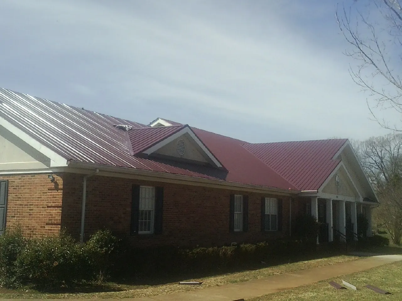 Red metal roof with gabled entries on a long brick building, from a Hail Damage Roof Repair job in Marcellus